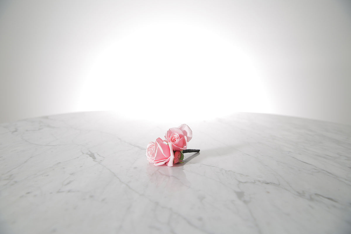 Kate Hill Flowers – pink spray rose buttonhole flowers with black-taped stem and pearl pin on a marble table setting.