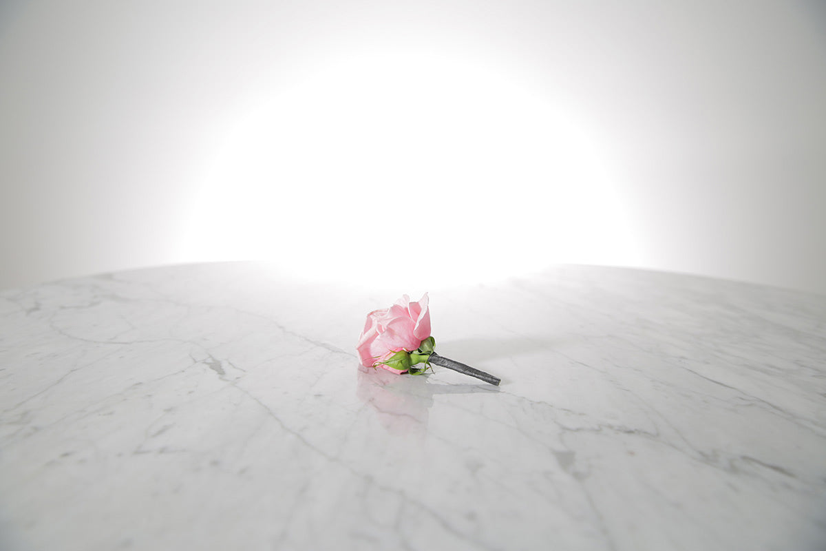 Kate Hill Flowers – pink spray rose buttonhole flowers with black-taped stem and pearl pin on a marble table setting.