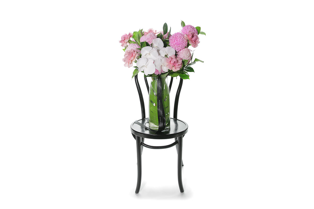 Kate Hill Flowers – large soft-pink celebration vase with roses, chrysanthemums and orchids in a monstera-lined glass.