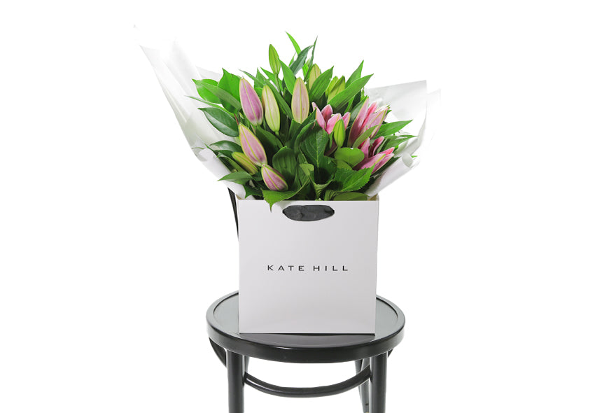 Medium to large sized pink lily bouquet sitting on a black bentwood chair. VARDA Lily Flower Bouquet features a simple bouquet of pink oriental Lilies and green seasonal foliage.