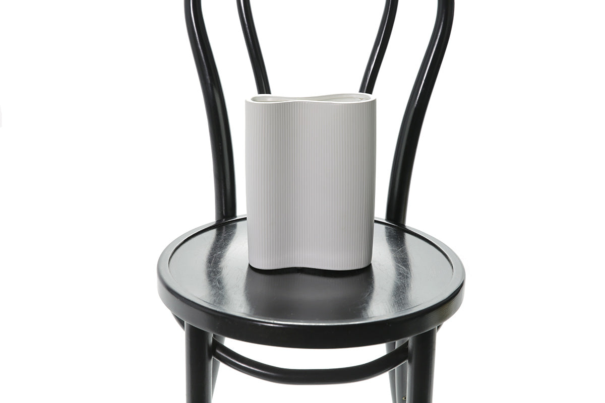 Close up image of white ceramic vase. A 22cm White ceramic wave vase sitting on black bentwood chair with white background.