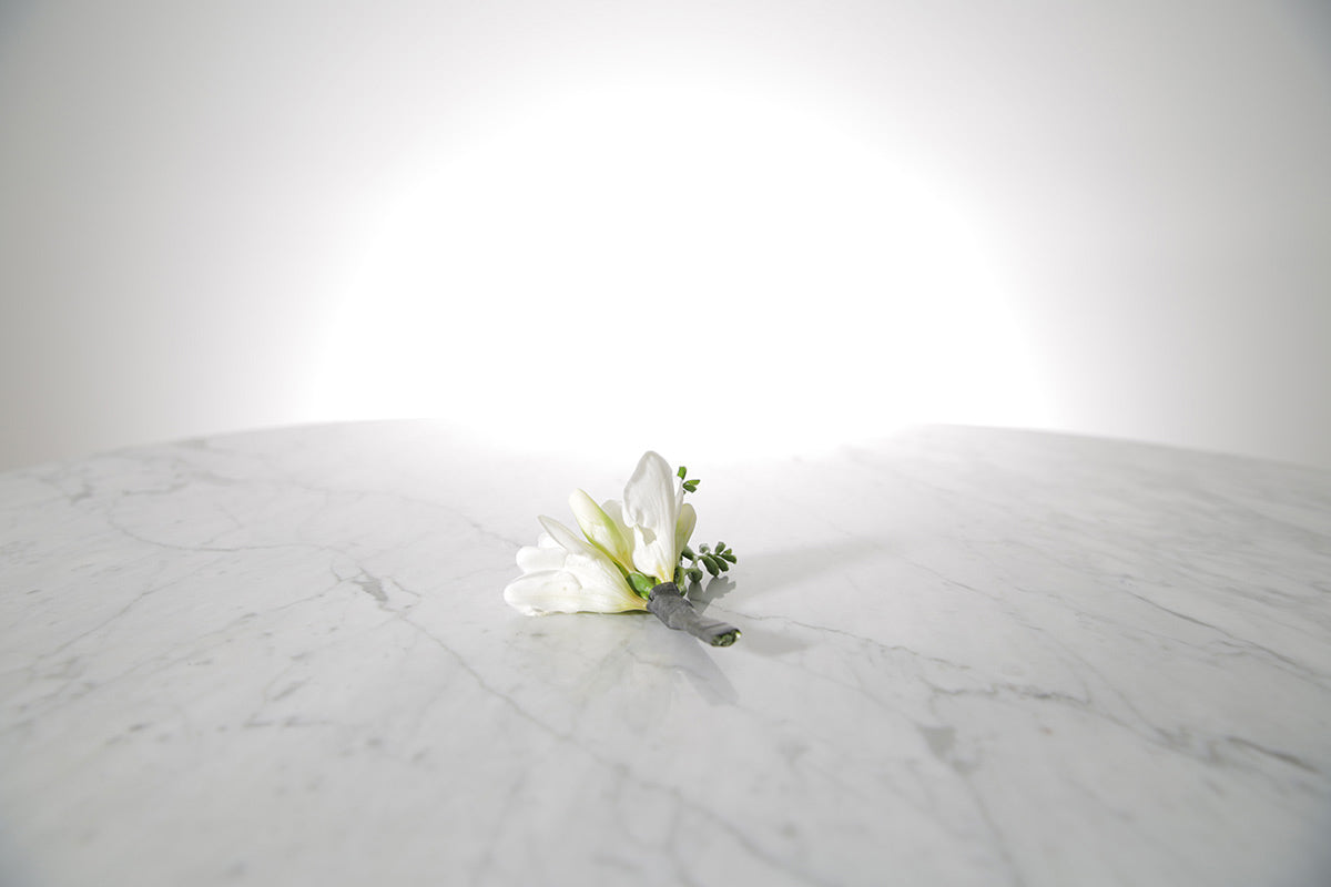 White floral freesia buttonhole on a marble surface with a light grey background