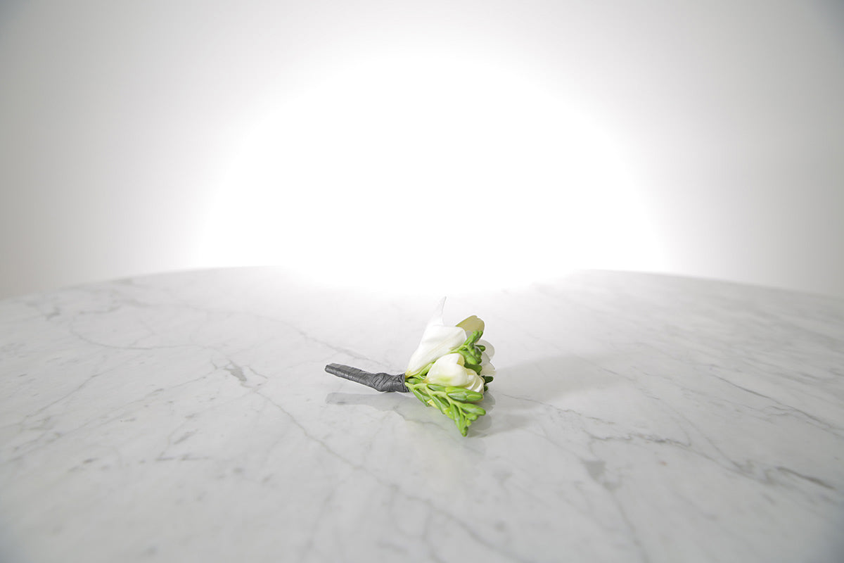 White freesia buttonhole flowers with a black holder on a marble surface