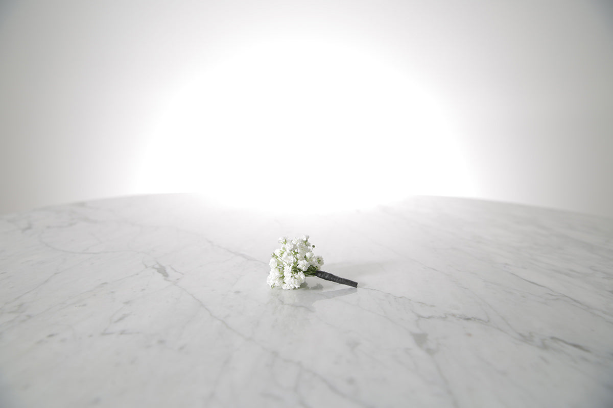 White flower boutonniere buttonhole flowers on a marble surface with a white background