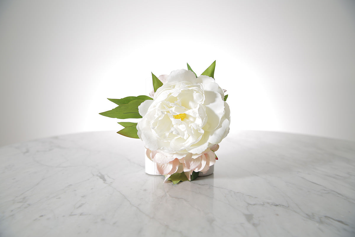 Kate Hill Flowers artificial white peony and blush hydrangea wrist corsage on silver elastic wristlet, displayed on a marble table with a white background.
