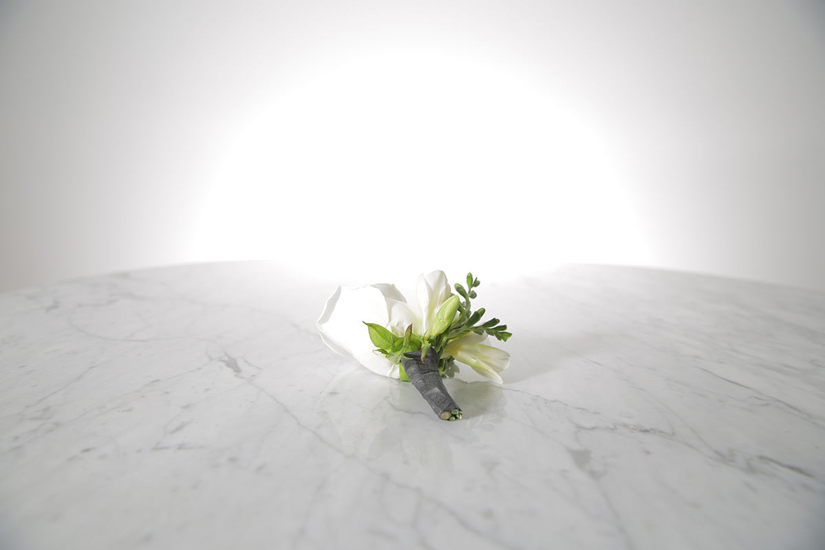 White rose and freesia buttonhole with black-taped stem and pearl pin with a light grey background