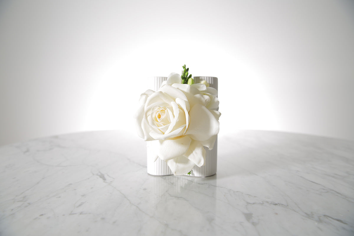 Kate Hill Flowers white rose and freesia wrist corsage on a silver elastic wristlet, boxed and ready to wear. Displayed on a marble table with a white background.