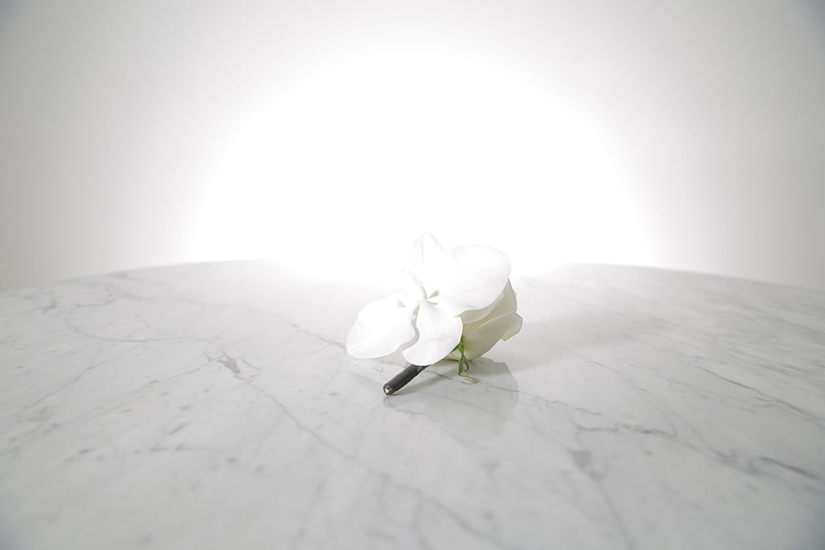White buttonhole flower on a marble surface with a light grey background