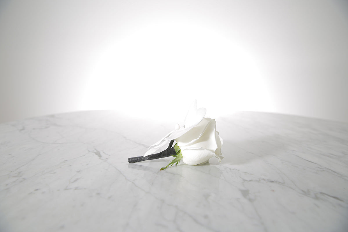 White rose buttonhole flower on a marble surface with a light grey background