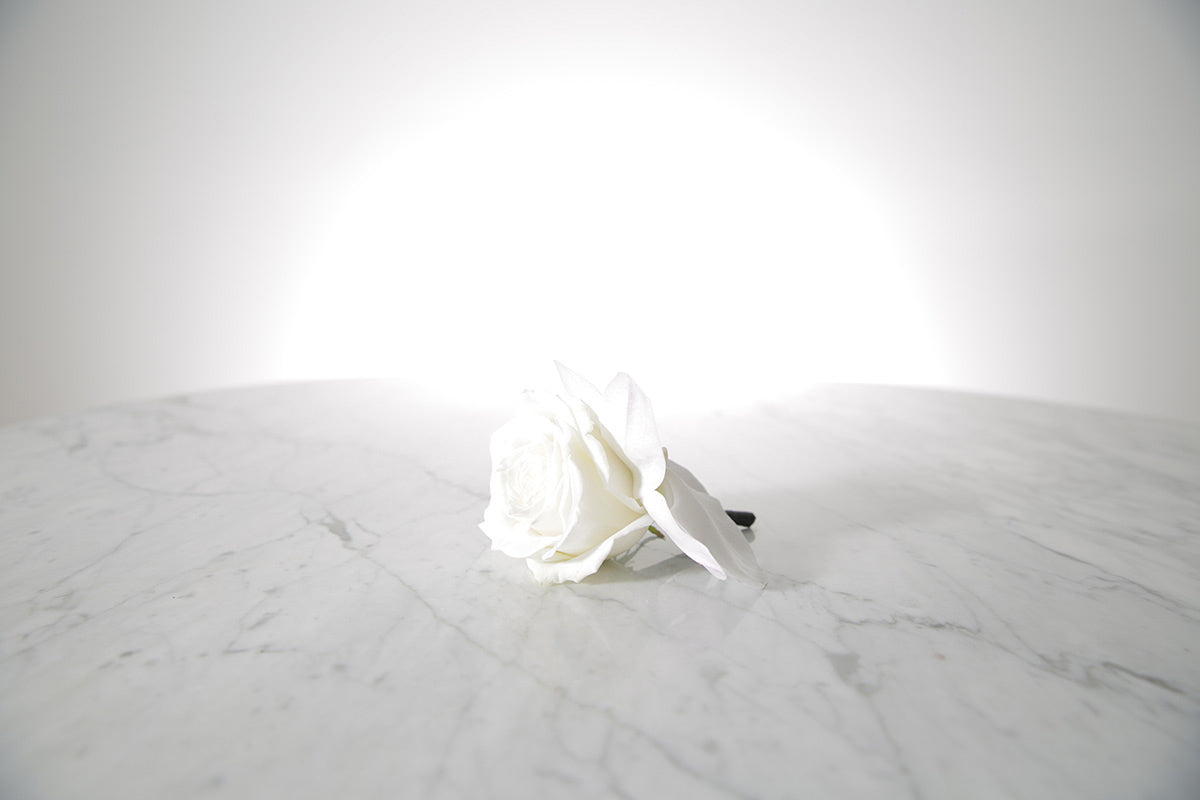 White rose buttonhole on a marble surface with a light grey background