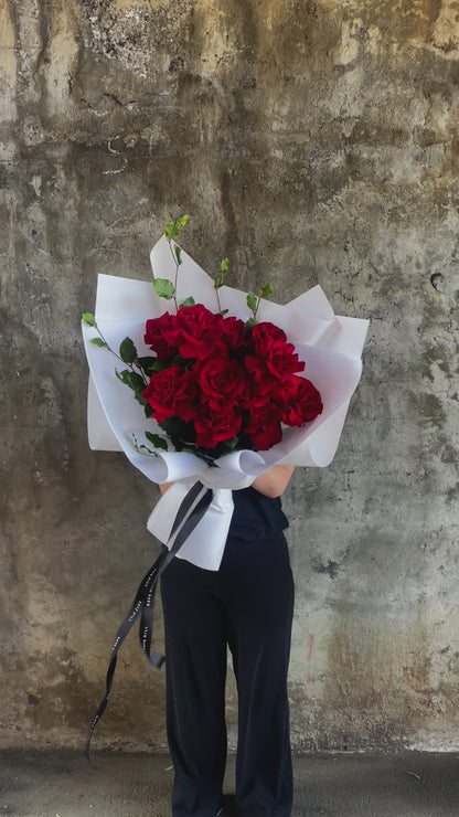 Video of florist holding one dozen red rose bouquet, with concrete wall in the background.
