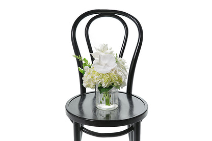 Petite ribbed glass vase displaying white and green seasonal flower. Gift includes the vase. BAILEY vase flower design is beautifully presented in our flower bag and detailed with Kate Hill ribbon. Small vase design is sitting on black bentwood chair.