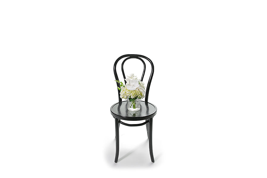 Wide image of the vase design sitting on the black bentwood chair to show honest size of the gift. Petite ribbed glass vase displaying white and green seasonal flower. Gift includes the vase. BAILEY vase flower design is beautifully presented in our flower bag and detailed with Kate Hill ribbon. Small vase design is sitting on black bentwood chair.