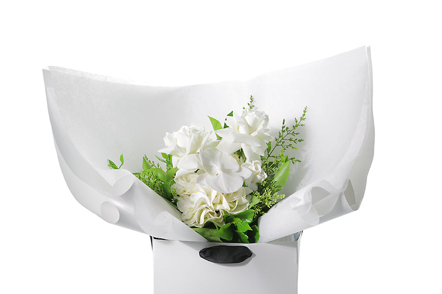 Close up image of the ELLA Flower Posy. ELLA white and green posy wrapped in signature Kate Hill flowers wrapping and placed into a flower bag. Bouquet bag is sitting on a black bentwood chair. Seasonal white and green posy.