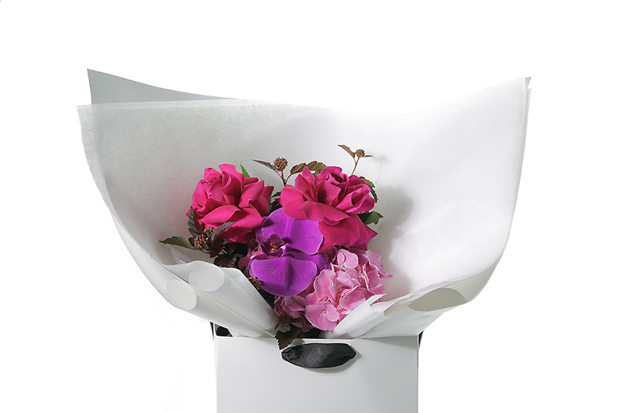 Close up image of the LENI flower bouquet. Small bright pink and magenta pink posy bouquet. Pink flowers and green seasonal foliage. Presented in Kate Hill Flower Bag. Bouquet bag is sitting on a black bentwood chair.
