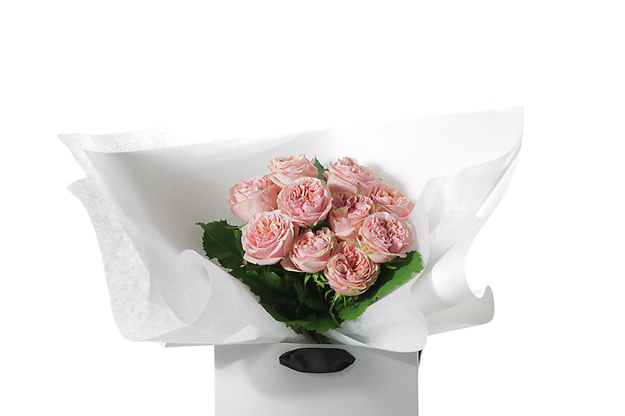 Close up image of the VERA rose flower bouquet. VERA is classed as a small sized, hand tied bouquet of 10 stems of Classic Roses (no additional foliage with roses only). Vera rose bouquet is beautifully wrapped in our signature wrapping and placed into our flower bag. Bouquet bag is sitting on a black bentwood chair.