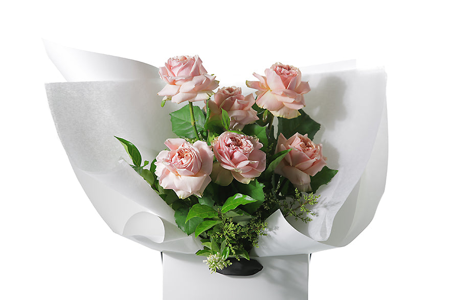 Close up image of the roses and bouquet. Classic rose bouquet featuring 6 stems of classic pink roses and green seasonal foliage. Gift bouquet presented in Kate Hill Flower Bag. Bouquet bag sitting on a black bentwood chair.