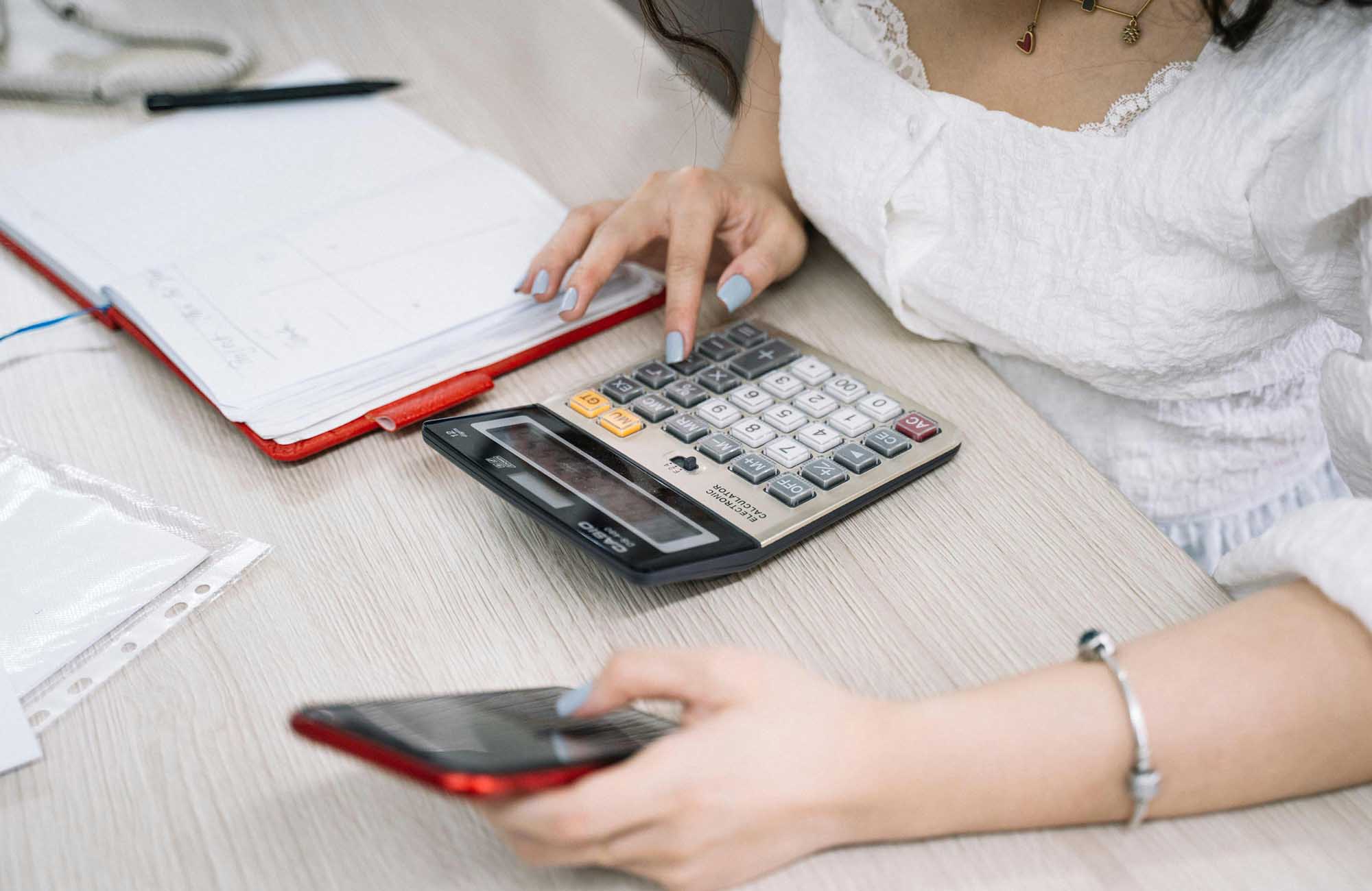 Lady in white dress using calculator and iPhone to work out wedding budget 
