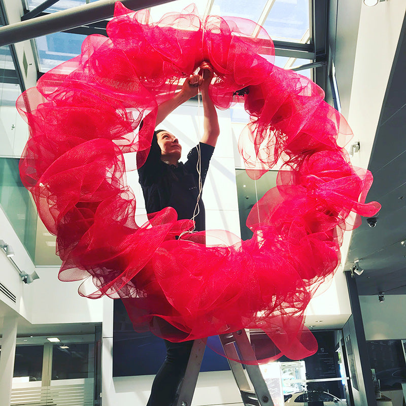 Melbourne Florist on ladder installing red Christmas wreath in business showroom