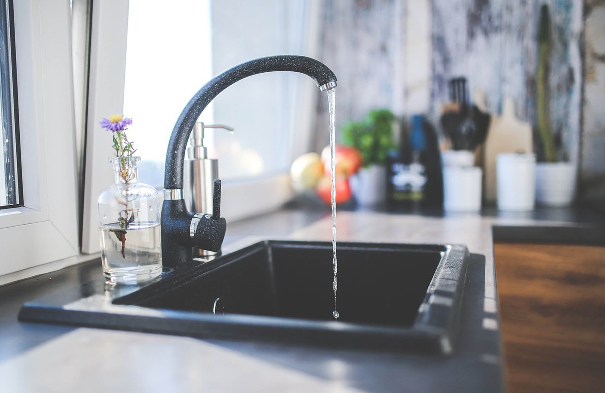 Flowers in a vase next to kitchen sink with water running