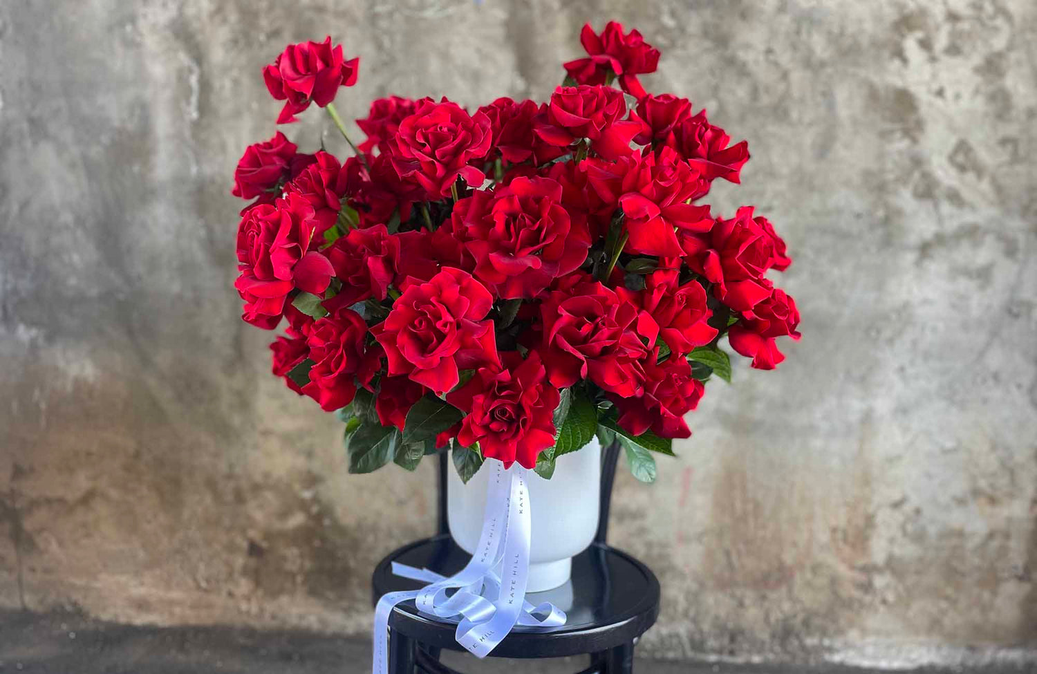 Large display of red Valentine's Day roses in a white container sitting on a black bent wood chair