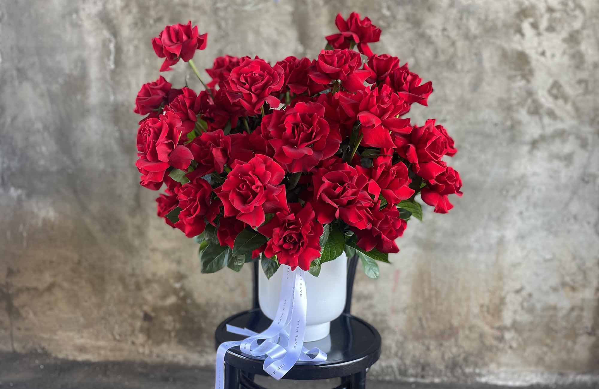 Large display of red Valentine's Day roses in a white container sitting on a black bent wood chair