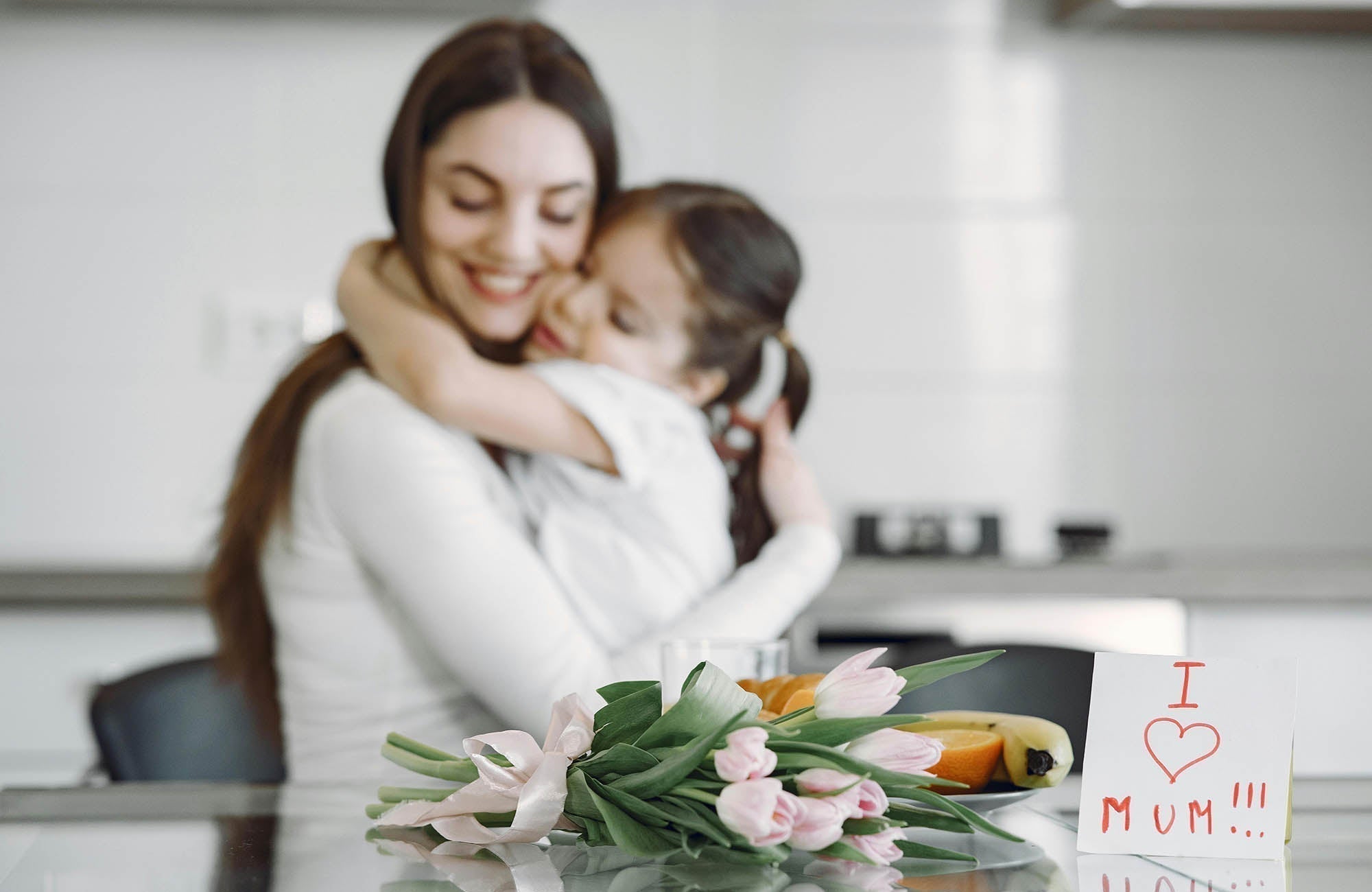 Mum with Mother's Day flowers given to her by her daughter hugging each other