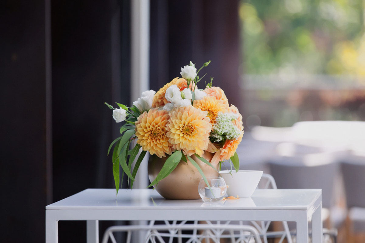 Summer flower table setting in Melbourne on a white table outdoors the vase contains flowers with orange hues, including Dahlia and Lisianthus