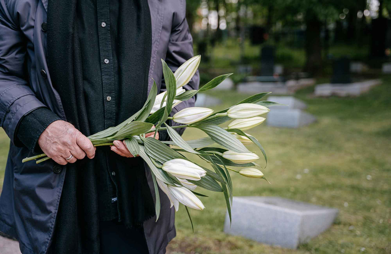 Man holding white lily Melbourne sympathy flowers in graveyard
