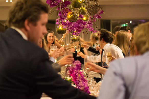 Guests with raised glasses and floral backdrop at wedding reception 