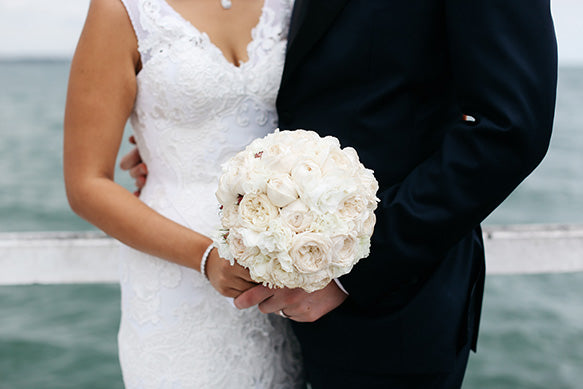Bride holding bridal bouquet by the waterside with husband