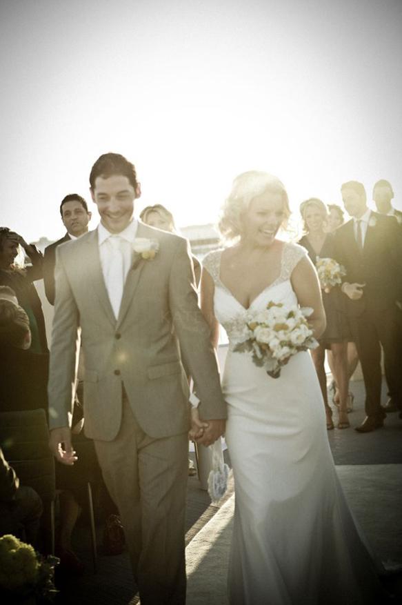 Newly wed bride and groom walking down isle after wedding ceremony smiling with bride holding her bridal bouquet 
