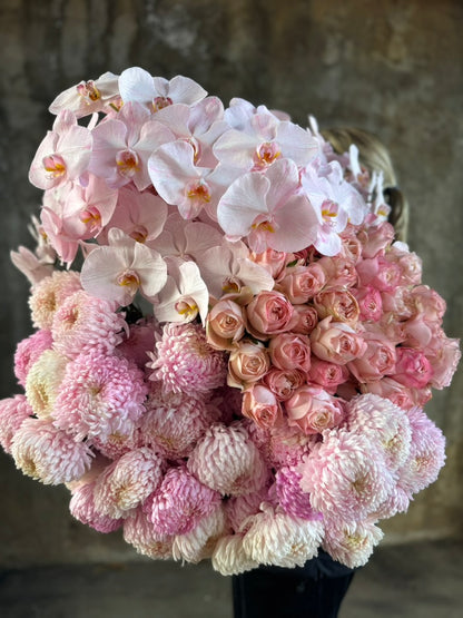 Close up image. A florist holding a large bundle of blush pink flowers against a concrete wall.