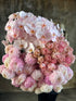 Close up image. A florist holding a large bundle of blush pink flowers against a concrete wall.