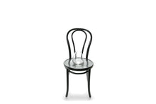 A 17cm glass mushroom vase sitting on a black bentwood chair with a white background.