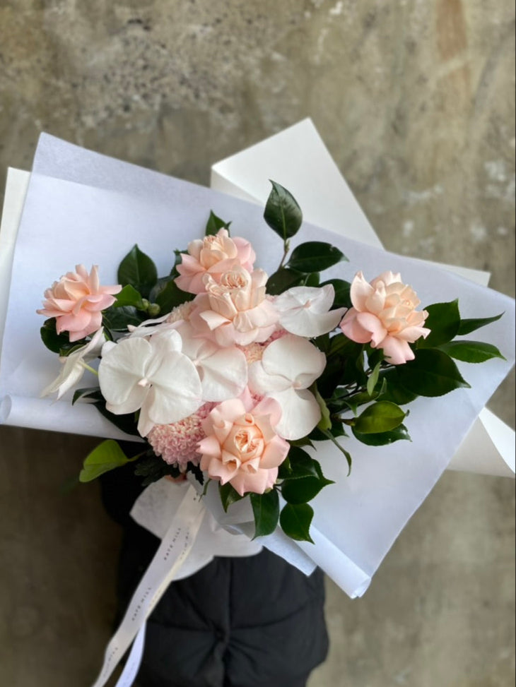 Close up image of blush flower bouquet held by a florist wearing black against a concrete grey wall.