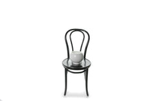 A 20cm white ceramic ball vase with foot sitting on a black bentwood chair with white background.