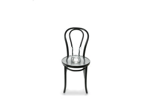 A 20cm glass compote vase sitting on a black bentwood chair with white background.