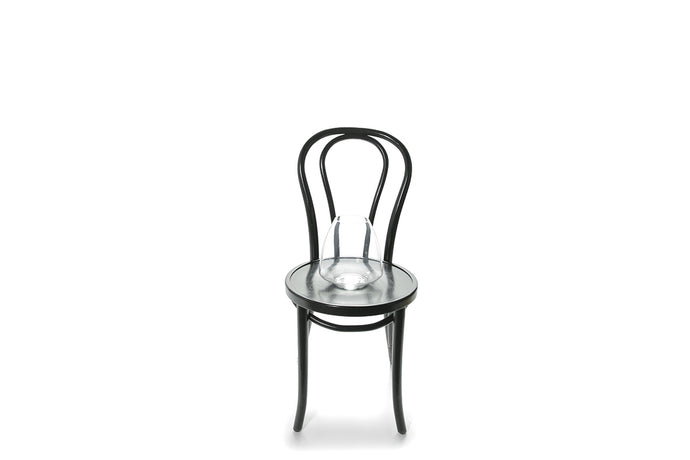 A 21cm mushroom glass vase sitting on a black bentwood chair with white background.