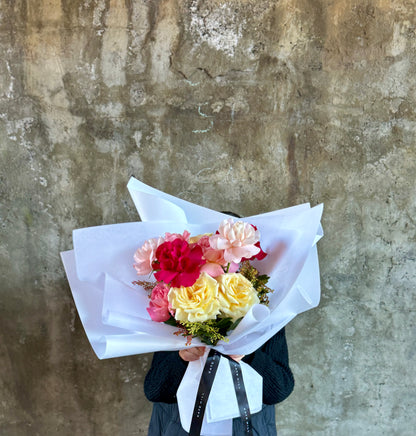 Florist holding the bouquet of mixed coloured roses and standing against a concrete wall.