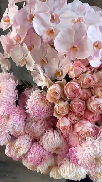 Video of flower bundle of blush flowers. A florist holding a large bundle of blush pink flowers against a concrete wall.