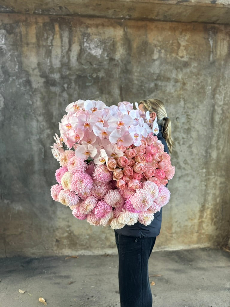 Wide Image of bundle of flowers. A florist holding a large bundle of blush pink flowers against a concrete wall.