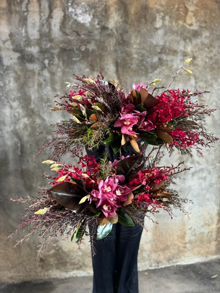 Florist holding 3 GARNET rich red tablescapes, against a concrete wall.