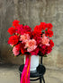 A large white vase displaying masses of orange, pink and watermelon roses which is sitting on a black bentwood chair against a concrete wall.