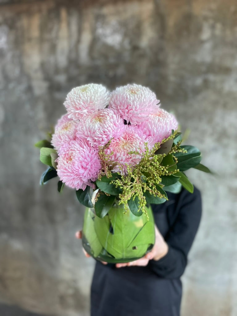 Close up image of florist holding the tapered vase design, displaying blush pink disbuds and green foliage.