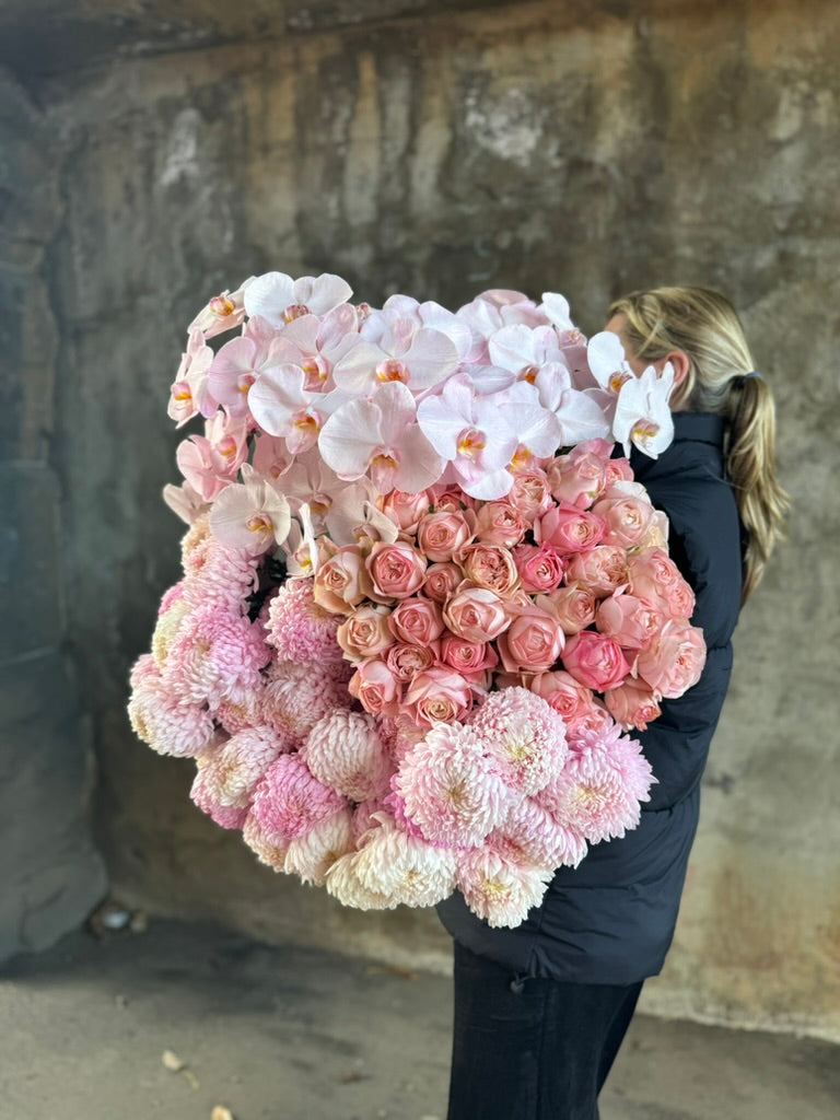 A florist holding a large bundle of blush pink flowers against a concrete wall.