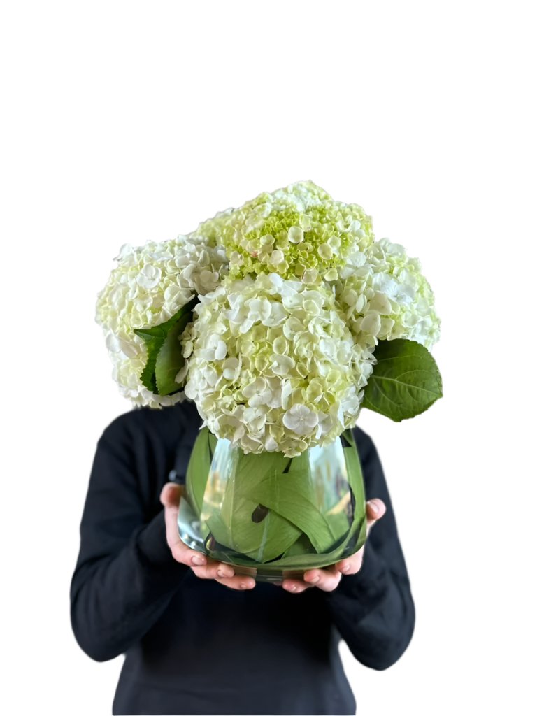 Florist holding tapered vase design with white hydrangeas. 