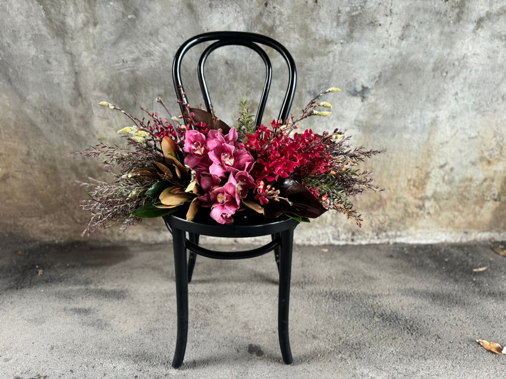 A black bentwood chair with the GARNET rich red tablescape sitting on chair, against a concrete wall.