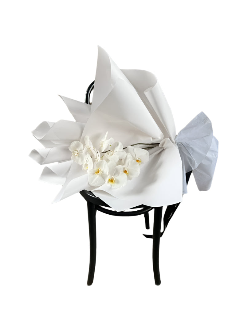White flowers wrapped in paper on a black chair against a textured wall.