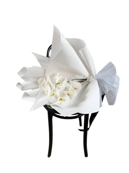 White flowers wrapped in paper on a black chair against a textured wall.